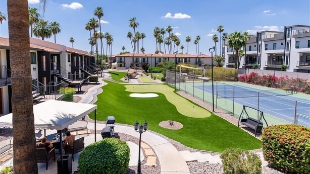 Un parcours de golf doté d’un green d’entraînement, d’un court de tennis et d’un espace extérieur aménagé avec des sièges.
