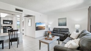 A modern living room with a sofa, coffee table, and a dining area with chairs and a kitchen in the background. - 128 Fully Furnished 1BR Suite-Prime Location! by RedAwning (Scottsdale)