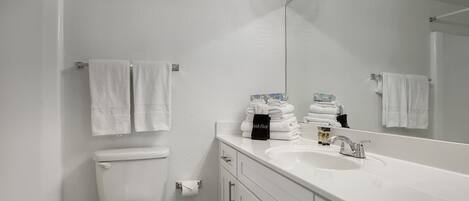 A modern bathroom with a white sink, mirror, and toilet. There are towels and toiletries on the counter.