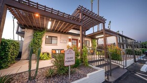 A guest parking area with a sign indicating it is for guests, a pergola structure, and a building with a white facade and a red door.