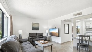 A modern living room with a grey sofa, a coffee table, a TV, and a kitchen area visible through an open door. - 244 Fully Furnished 1BR Suite-Pet Friendly! by RedAwning (Scottsdale)
