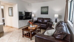 Ein Wohnzimmer mit Flachbildfernseher, Ledersofas, einem Couchtisch und einem fenster mit Vorhängen.