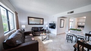 A modern living room with a sofa, a coffee table, and a TV. There is a kitchen area with a sign that says "Welcome". - 202 Fully Furnished with WiFi by RedAwning (Scottsdale)