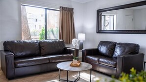 A modern living room with a brown leather sofa, a round coffee table, and a large mirror on the wall. - 202 Fully Furnished with WiFi by RedAwning (Scottsdale)