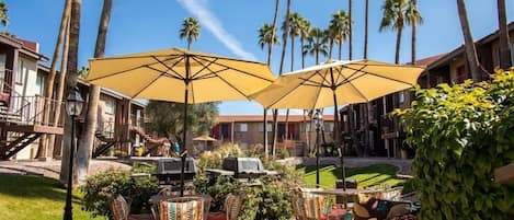 An outdoor patio with yellow umbrellas, wicker chairs, and a grill.
