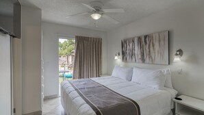 Ein Hotelzimmer mit Bett, Deckenventilator, einem Gemälde an der Wand und Blick ins Freie.