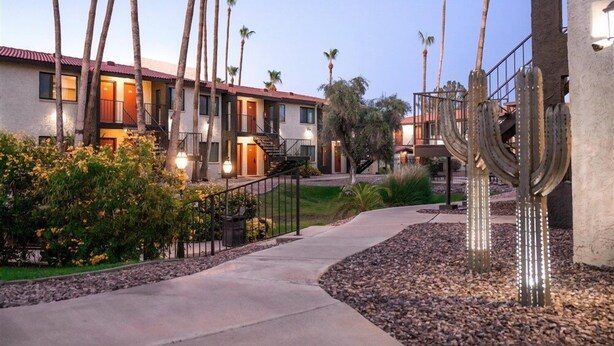 A residential area with multiple two-story houses, a paved walkway, and palm trees.