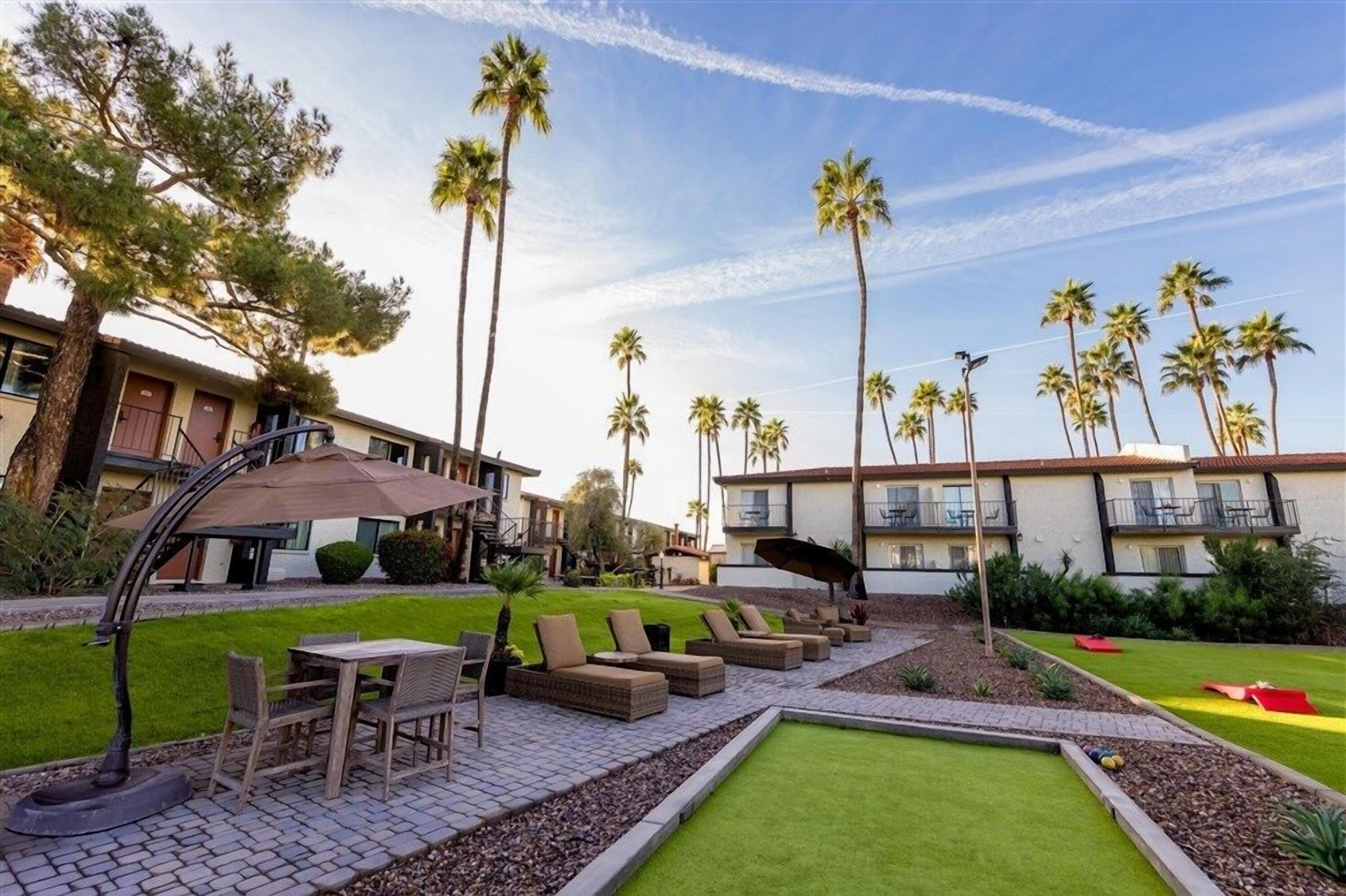 A hotel courtyard with outdoor seating, palm trees, and a well-maintained lawn.