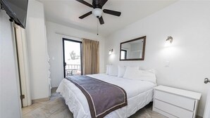 Ein Hotelzimmer mit Bett, Nachttisch, Deckenventilator, einem Fenster mit Vorhängen und einer Tür zum Balkon.