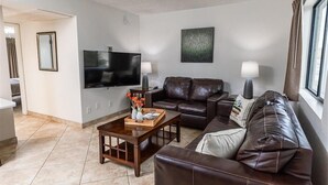 A living room with a TV, leather sofas, a coffee table, and a window with curtains. - 116 Fully Furnished 1BR Suite-Prime Location! by RedAwning (Scottsdale)