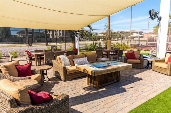 An outdoor patio area with wicker furniture, a wooden coffee table, and a large canopy providing shade.