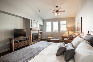 A hotel room with a large bed, a television, a fireplace, a ceiling fan, and a window with blinds. - Fraser Crossing/Founders Pointe, Condo | 2 bedroom King Beds & Washer/Dryer (Premium Rated Condo 4449) (Winter Park)