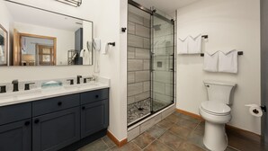 A modern bathroom with a glass-enclosed shower, a white toilet, and a dark-colored vanity with a mirror. - Zephyr Mountain Lodge, Condo | 2 bedroom, Gas Fireplace & Continental Divide Views (Premium Rated Condo 1701) (Winter Park)