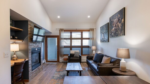 A modern living room with a fireplace, a sofa, a coffee table, and a dining area with a lamp. - Zephyr Mountain Lodge, Condo | 2 bedroom, Gas Fireplace & Continental Divide Views (Premium Rated Condo 1701) (Winter Park)