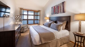 A bedroom with a large bed, a dresser, a window with blinds, and a painting on the wall. - Zephyr Mountain Lodge, Condo | 2 bedroom, Gas Fireplace & Continental Divide Views (Premium Rated Condo 1701) (Winter Park)