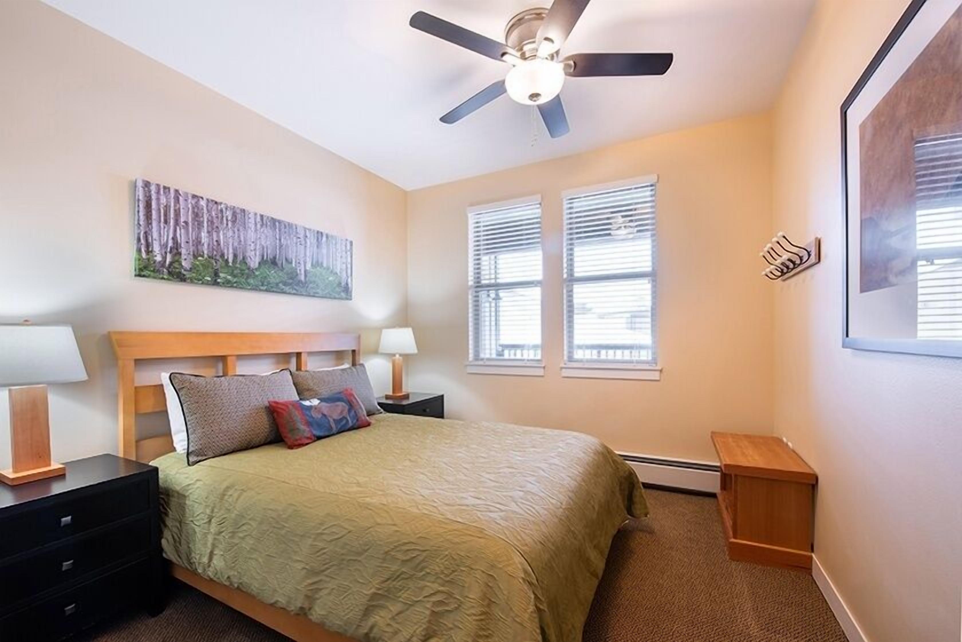 Un dormitorio con cama, mesitas de noche, ventilador de techo y ventana con persianas.