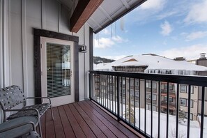 En træterrasse med gelænder i metal, en bænk og en dør med skodder.