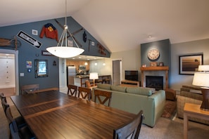 A modern living room with a dining area, a fireplace, and a kitchen in the background.