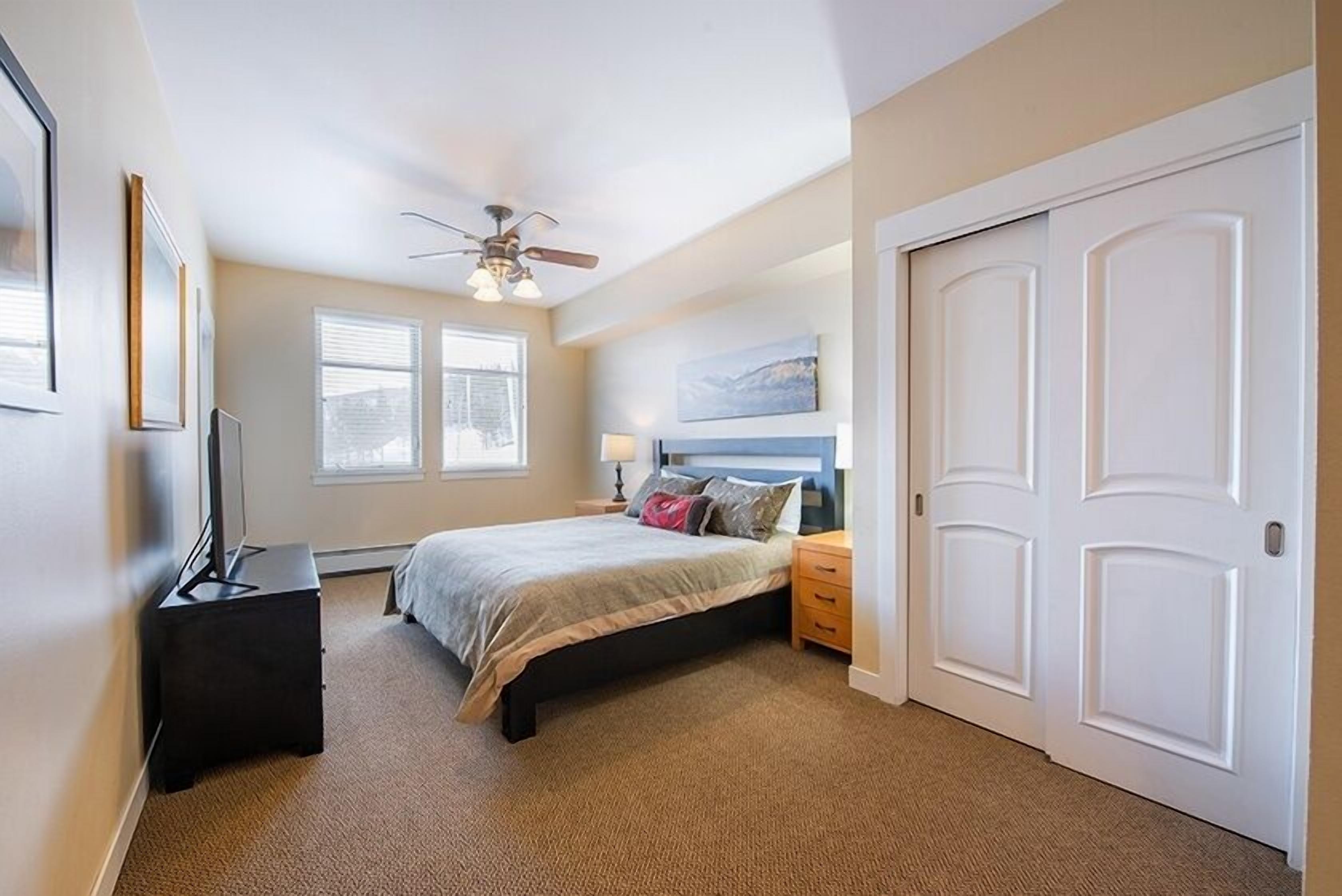 Een slaapkamer met een bed, een plafondventilator, een dressoir, een nachtkastje en een deur.