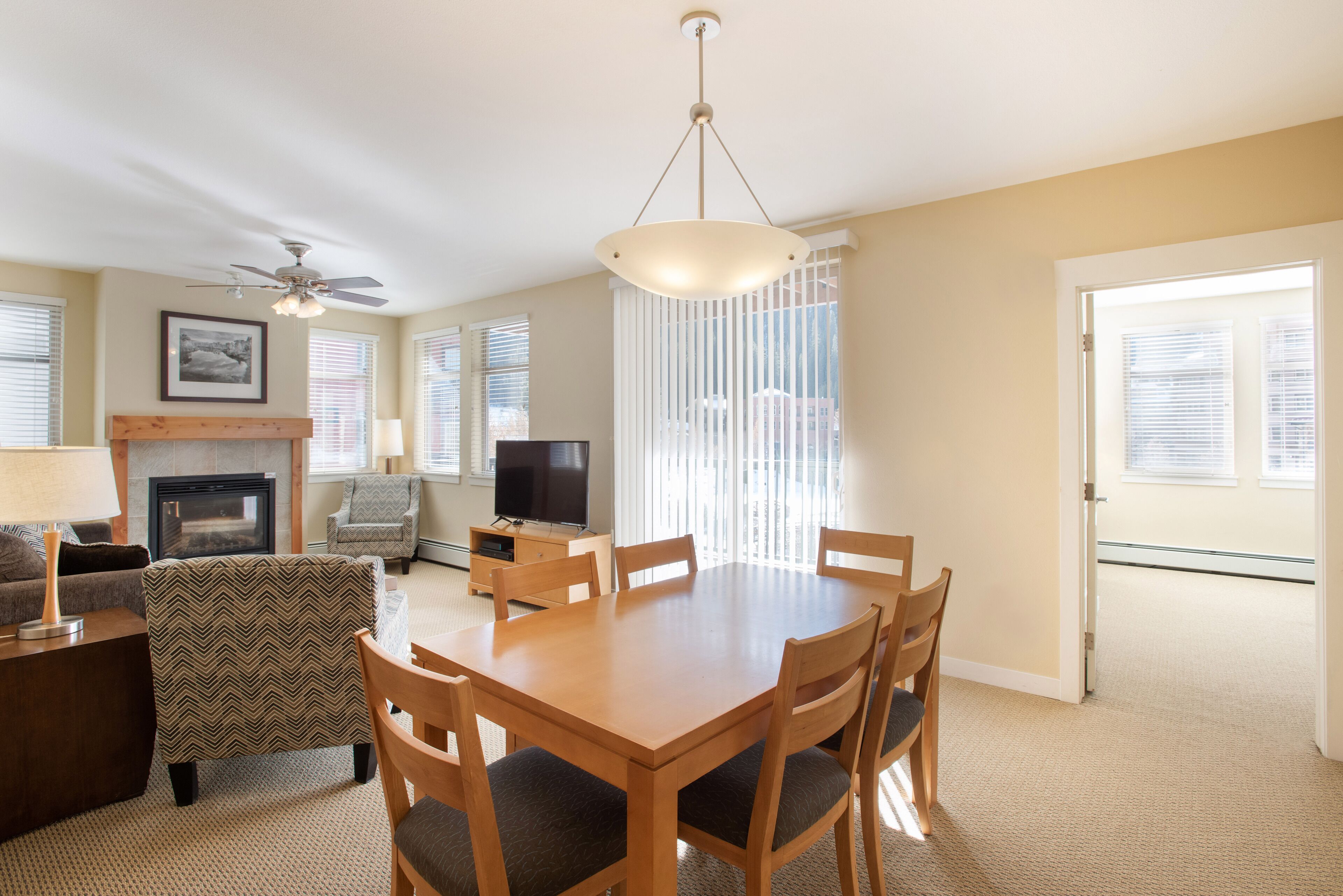 A living room with a fireplace, a television, a dining table with chairs, and a ceiling fan.