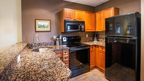 Une cuisine dotée de plans de travail en granit, de meubles en bois, d’un évier en acier inoxydable, d’une cuisinière noire, d’un four à micro-ondes noir et d’un réfrigérateur noir.
