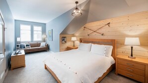 A bedroom with a large bed, wooden headboard, two bedside tables with lamps, a wooden bench, and a window with blinds. - Fraser Crossing/Founders Pointe, Condo | 3 bedroom Ski Slope Views (Select Rated Condo 3625) (Winter Park)