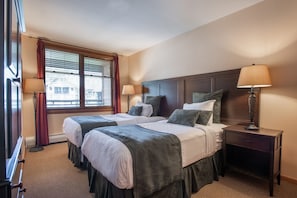 A hotel room with two beds, a nightstand, and a window with blinds.