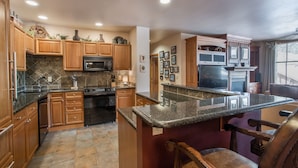 A kitchen with wooden cabinets, granite countertops, a built-in oven, and a large island with bar stools.
