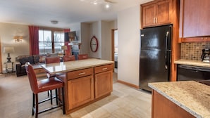 A modern kitchen with wooden cabinets, a black refrigerator, and a granite countertop.