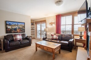 A living room with two leather sofas, a wooden coffee table, a painting on the wall, and a window with blinds. - Zephyr Mountain Lodge, Condo | 3 Bedroom (Premium-Rated Condo 2323) (Winter Park)