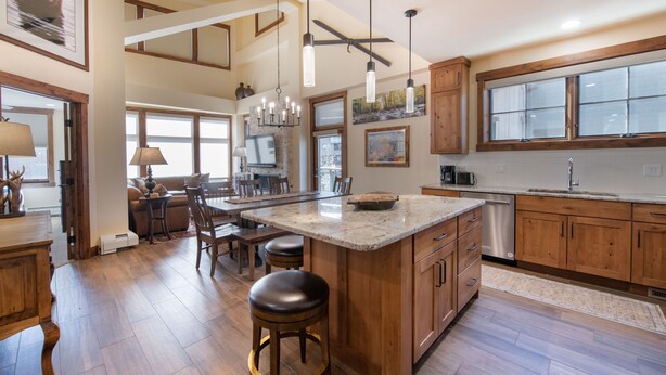 A spacious kitchen with wooden cabinets, a large island with stools, and pendant lighting.