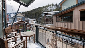 A balcony with wooden furniture, a view of a ski resort, and a sign for 'Winter Park Rentals'.