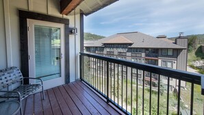 A wooden deck with a bench and a door with blinds, overlooking a multi-story building with balconies. - Fraser Crossing/Founders Pointe, Condo , Gondola Access (Select-Rated Condo 4654) (Winter Park)