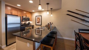 A modern kitchen with a central island, stainless steel appliances, pendant lighting, and a ski rack on the wall. - Fraser Crossing/Founders Pointe, Condo | 2 Bedroom (Value-Rated Condo 3426) (Winter Park)