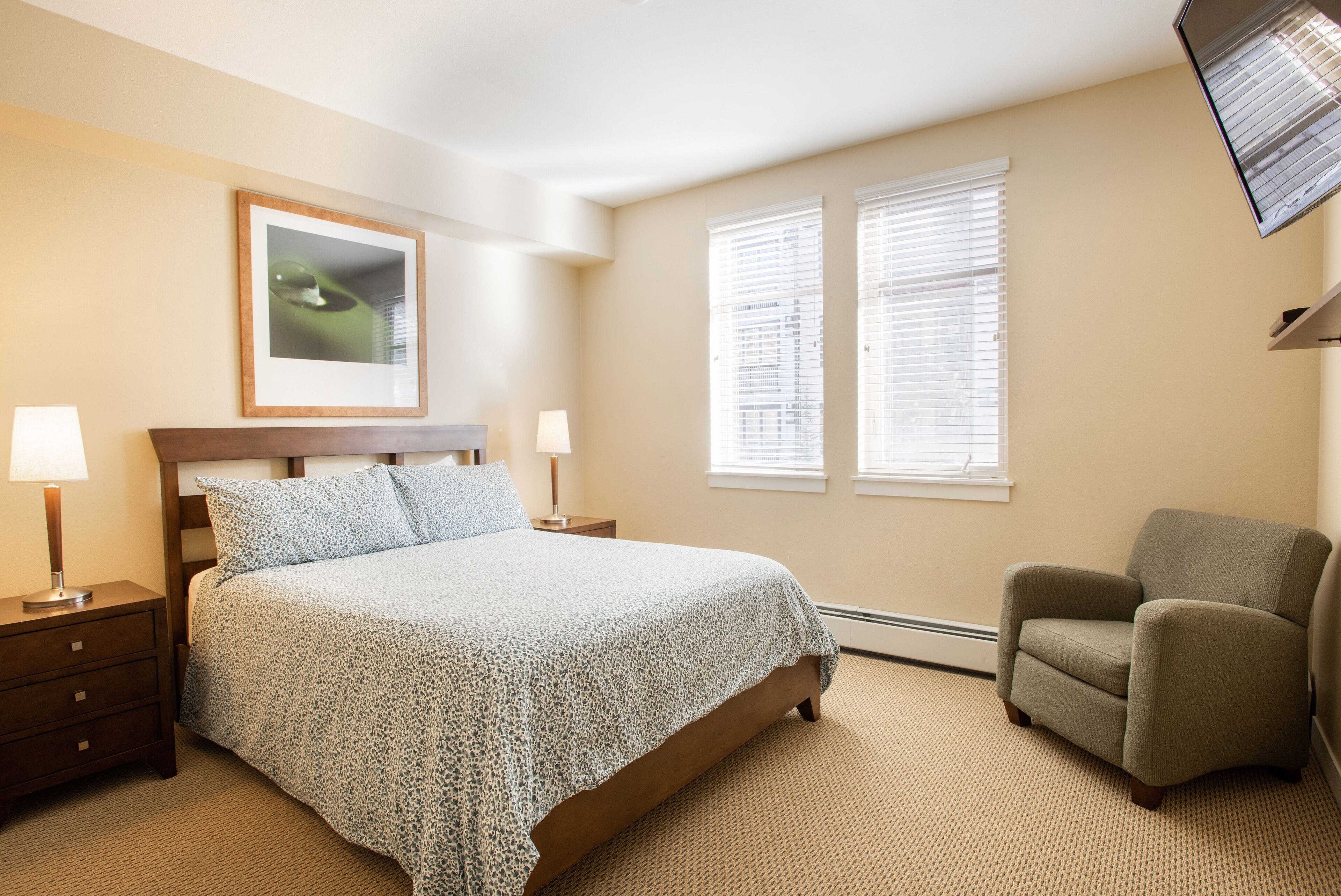 A bedroom with a bed, two bedside tables with lamps, a chair, and a window with blinds.