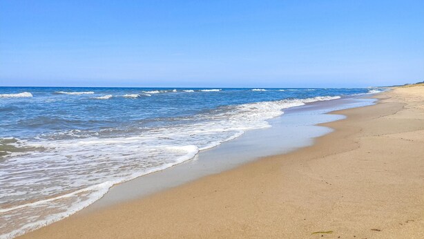 Een zandstrand met zachte golven en een helderblauwe lucht.