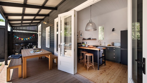 A modern kitchen with a wooden island, a dining area with a table and chairs, and a covered outdoor space with a grill. - The Elm Tree- Designer Home in the heart of Daylesford (Daylesford)