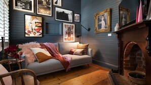A cozy living room with a grey sofa, a fireplace, and various framed artworks on the wall. - The Elm Tree- Designer Home in the heart of Daylesford (Daylesford)