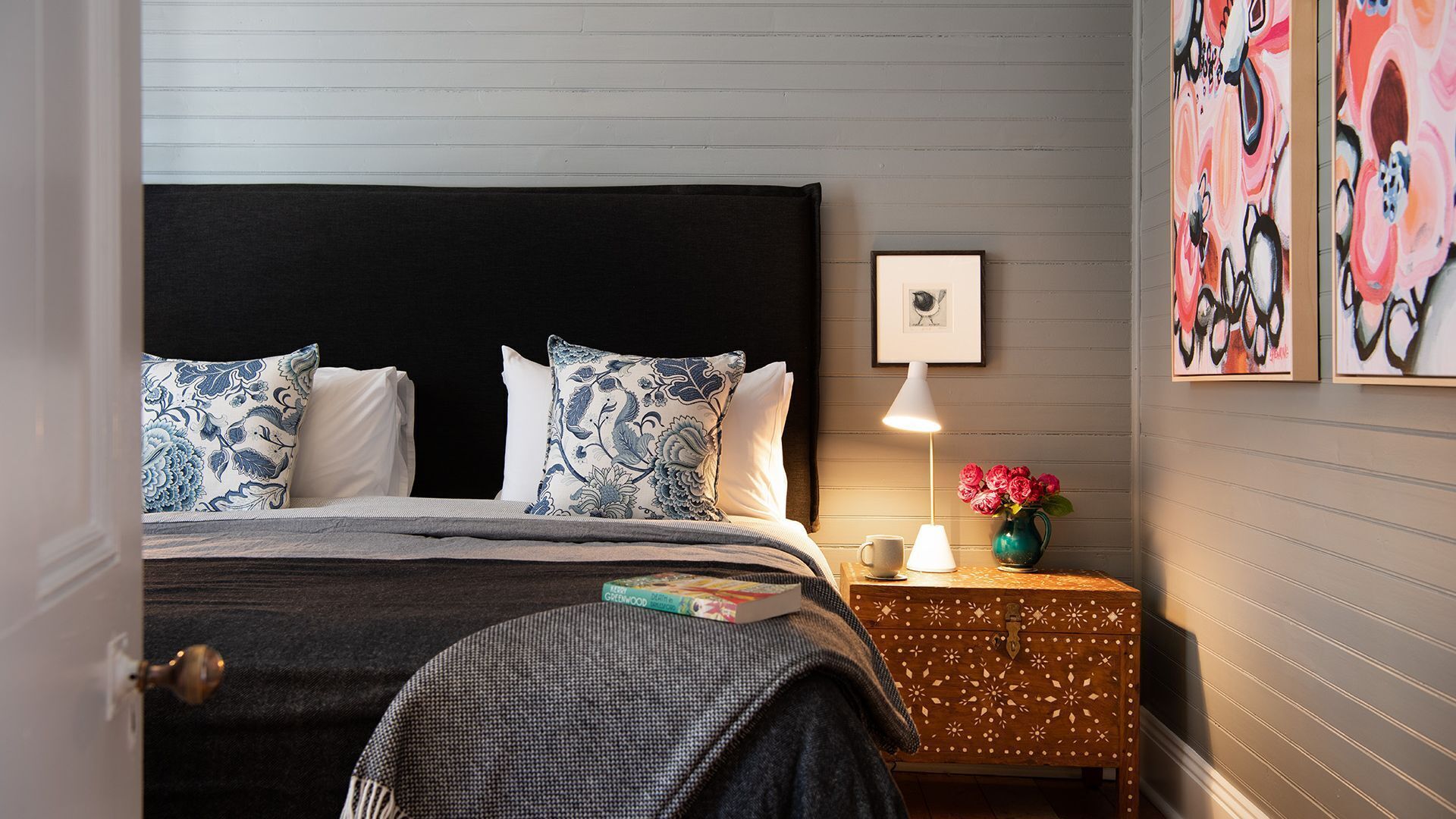 A neatly arranged bedroom with a bed, bedside table, lamp, and artwork.