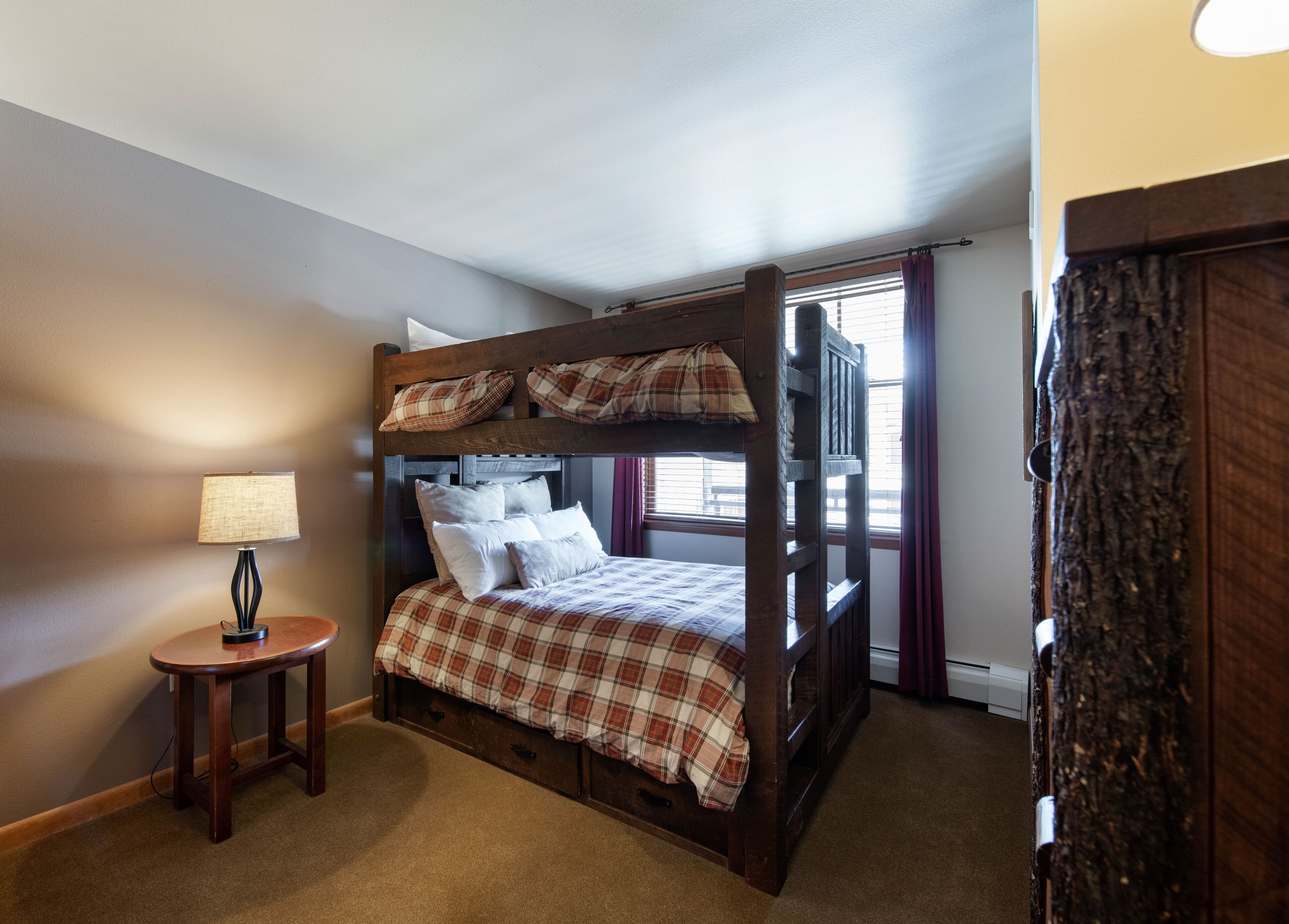 A bunk bed with a plaid bedspread, a bedside lamp, and a small wooden table.