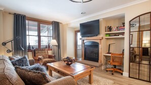 A living room with a fireplace, a television mounted above it, and a bookshelf filled with books and decorative items. - Zephyr Mountain Lodge, Condo | 2 Bedroom (Select-Rated Condo 1315) (Winter Park)