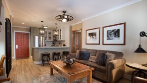 A modern living room with a wooden coffee table, a sofa with decorative pillows, and a kitchen area with bar stools. - Zephyr Mountain Lodge, Condo | 2 Bedroom (Select-Rated Condo 1315) (Winter Park)