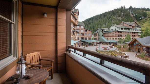 Un balcon doté de meubles en bois, offrant une vue sur une zone touristique avec des bâtiments et une montagne en arrière-plan.