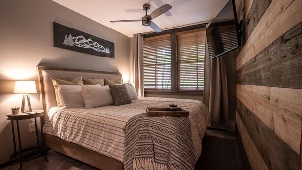 A bedroom with a bed, a nightstand, a ceiling fan, a window with blinds, and a wall-mounted TV. - Zephyr Mountain Lodge, Condo | 1 Bedroom (Premium-Rated Condo 1205) (Winter Park)