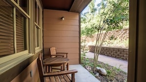 Un banc et une table en bois, installés sur une terrasse couverte, offrent une vue sur un mur de briques et sur la verdure.