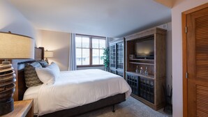 Un dormitorio con una cama, televisión, aparador de madera y ventana.
