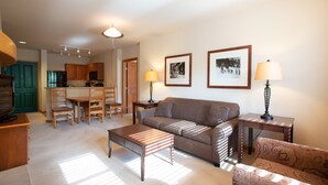 A living room with a sofa, a coffee table, and a patterned armchair. There is a dining area with wooden chairs and a table, and a kitchen with wooden cabinets and a refrigerator. - Zephyr Mountain Lodge, Condo | Ski Slope View (Select-Rated Condo 2405) (Winter Park)