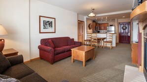 A living room with a red sofa, a wooden coffee table, and a dining area with chairs and a table. - Zephyr Mountain Lodge, Condo | Ski-In/Ski-Out w/ Balcony Views (Value-Rated Condo 1516) (Winter Park)