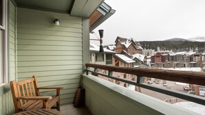 A balcony with a wooden bench and a table, overlooking a town with snow-covered buildings and a mountain in the background. - Zephyr Mountain Lodge, Condo | Ski-In/Ski-Out w/ Balcony Views (Value-Rated Condo 1516) (Winter Park)