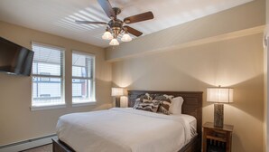 A bedroom with a bed, a ceiling fan, a nightstand with a lamp, and a TV mounted on the wall. - Fraser Crossing/Founders Pointe, Condo | Gondola Access (Premium-Rated Condo 3624) (Winter Park)